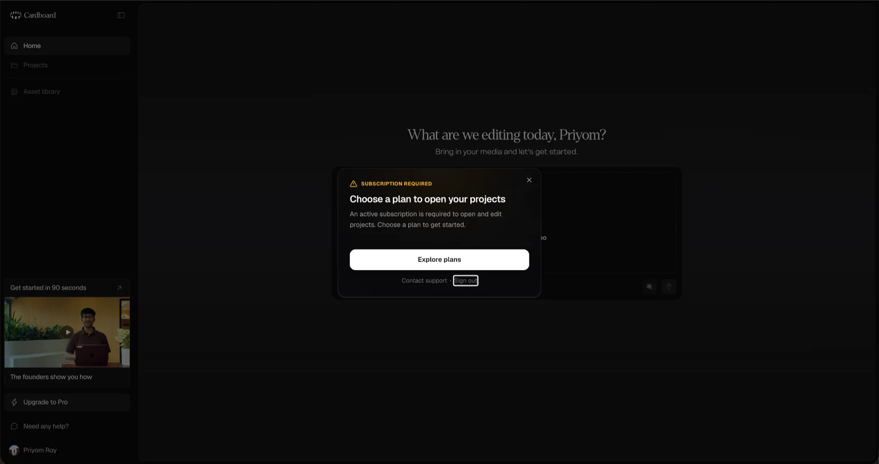 A dialog over the dimmed Cardboard home screen. In amber small capitals, "SUBSCRIPTION REQUIRED", then the heading "Choose a plan to open your projects" and the line "An active subscription is required to open and edit projects. Choose a plan to get started." A white "Explore plans" button fills the width, with "Contact support" and "Sign out" beneath it. In the sidebar behind, Projects and Asset library are still lit and still clickable, and a founders’ walkthrough video sits above "Upgrade to Pro".